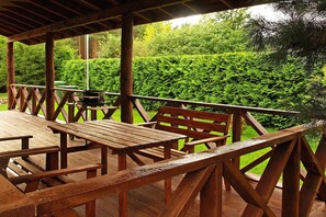 An outdoor wooden deck with picnic tables and benches, surrounded by lush greenery. - Year-round Holiday Home With Fireplace, 3 Bedrooms (Choczewo)