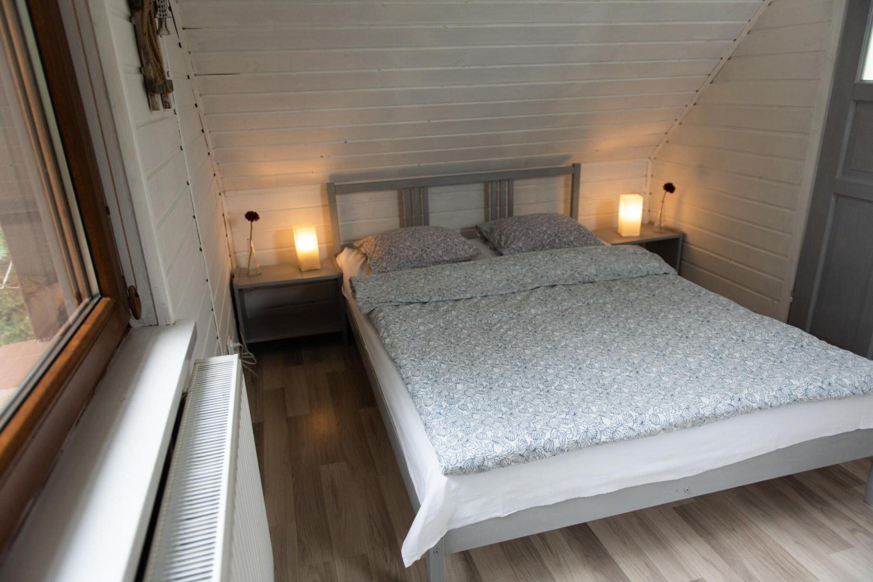 Ein Einzelbett in einem Zimmer mit schrägem Dach, zwei Nachttische mit Lampen und ein Fenster auf der linken Seite.
