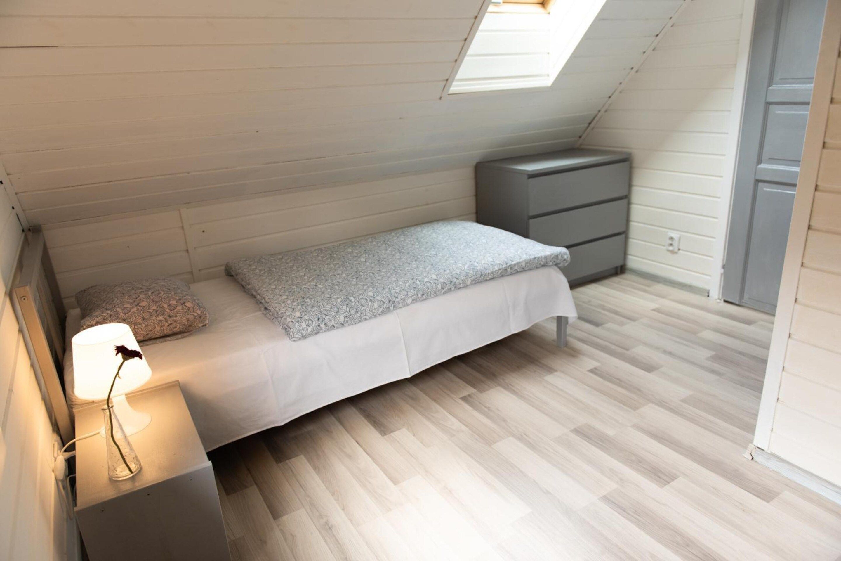 Un dormitorio pequeño y ordenado con una cama individual, una mesita de noche con lámpara y un aparador.