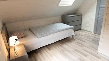 Un dormitorio pequeño y ordenado con una cama individual, una mesita de noche con lámpara y un aparador.