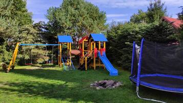 Un parque infantil con tobogán, columpios y cama elástica.