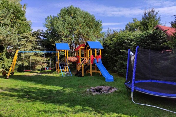 Une aire de jeux avec un toboggan, des balançoires et un trampoline.