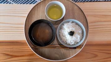 A wooden tray with a bowl of white rice, a small bowl of soy sauce, and a cup of tea on a wooden table.