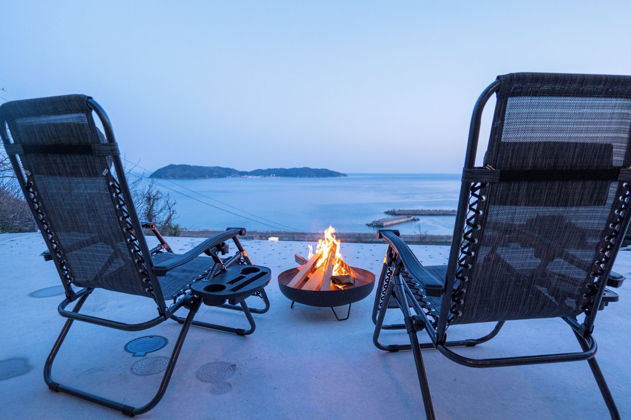 Two outdoor chairs facing a fire pit with a view of the sea.