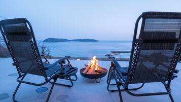 Two outdoor chairs facing a fire pit with a view of the sea.