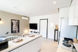 A modern kitchen with a central island, a flat-screen TV mounted on the wall, and a statue on a pedestal. - Atlas, a Modern Cocoon in the Heart of La Marsa (La Marsa)