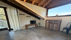 A room with a stone floor, a wooden bench, a TV, a wooden table with stools, and a view through a window. - Enchantment of the Lake app Palanzo Studio Apartment with Terrace A/C (Molina)