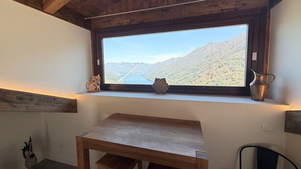 A room with a wooden table, a window with a mountain view, and a vase on the windowsill. - Enchantment of the Lake app Palanzo Studio Apartment with Terrace A/C (Molina)