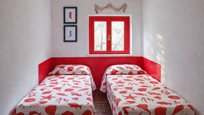 Una stanza con due letti, una finestra con persiane rosse e un elemento decorativo a parete.