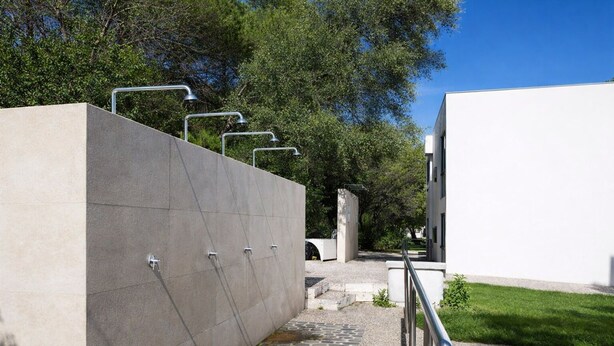 Un edificio moderno con facciata in cemento, un vialetto in pietra, ringhiere in metallo e un'area verde.