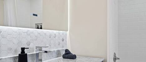 A bathroom with a white sink, a mirror, a towel, and a shower.