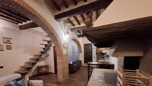 Ein rustikales Interieur mit freiliegenden Backsteinwänden, einem Kamin aus Stein, einer Holztreppe und einer gemütlichen Sitzecke.
