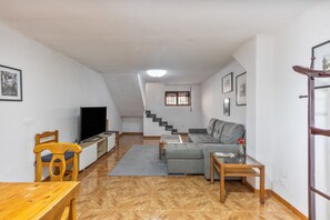 A living room with a sofa, a TV, a wooden table, and a staircase leading to another level.