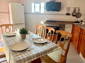 Une cuisine équipée d’une table à manger pour deux personnes, d’un réfrigérateur, d’une cuisinière et d’un téléviseur fixé au mur.