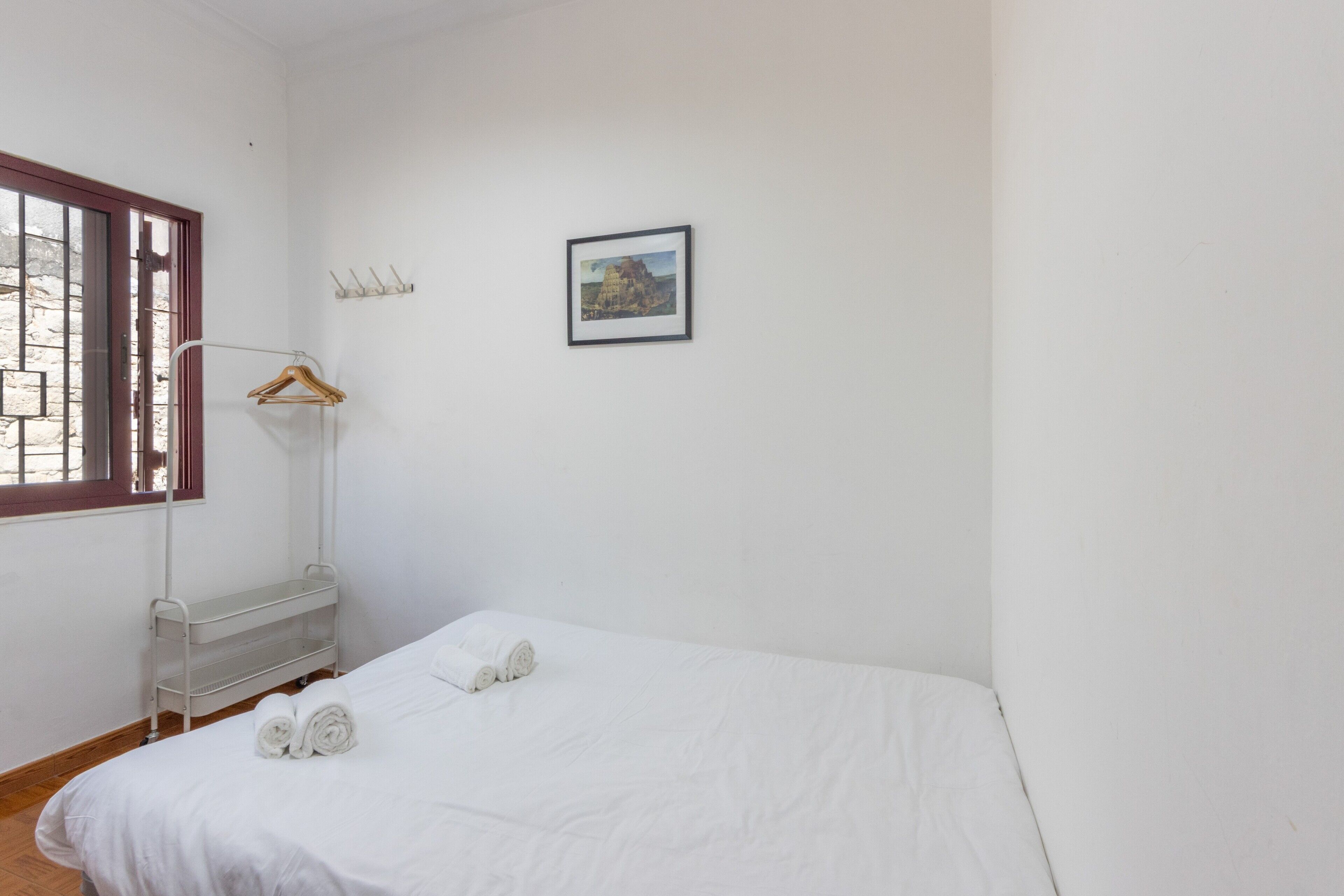 Una stanza semplice e pulita con un letto singolo, una finestra vista e un quadro appeso al muro.