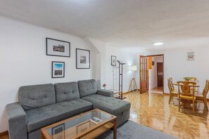 A living room with a grey sofa, a glass coffee table, and a dining area with wooden chairs and a table. - Family Retreat 5 Minutes’ Walk from D. Luís I Bridge (Vila Nova de Gaia)