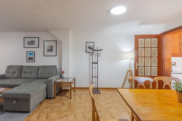 A living room with a sofa, a dining table with chairs, a lamp, and framed pictures on the wall.