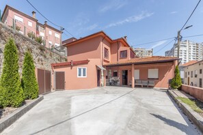 A two-story residential building with a garage, a patio with outdoor furniture, and a stone retaining wall. - Family Retreat 5 Minutes’ Walk from D. Luís I Bridge (Vila Nova de Gaia)