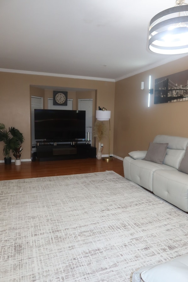 A living room with a flat-screen TV, a white sofa, a patterned rug, and a tall floor lamp.