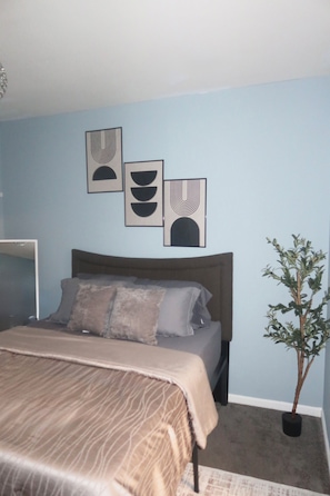 A bedroom with a bed, a potted plant, and three wall art pieces.