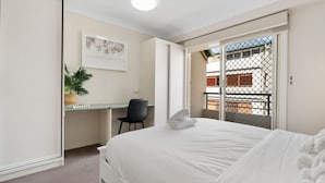 Quarto de hotel com cama, escrivaninha, cadeira, planta e vista para o exterior.