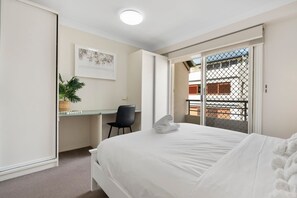 A hotel room with a bed, a desk, a chair, a plant, and a view of the outside. - Comfortable Stay With Pool Access (Brisbane)