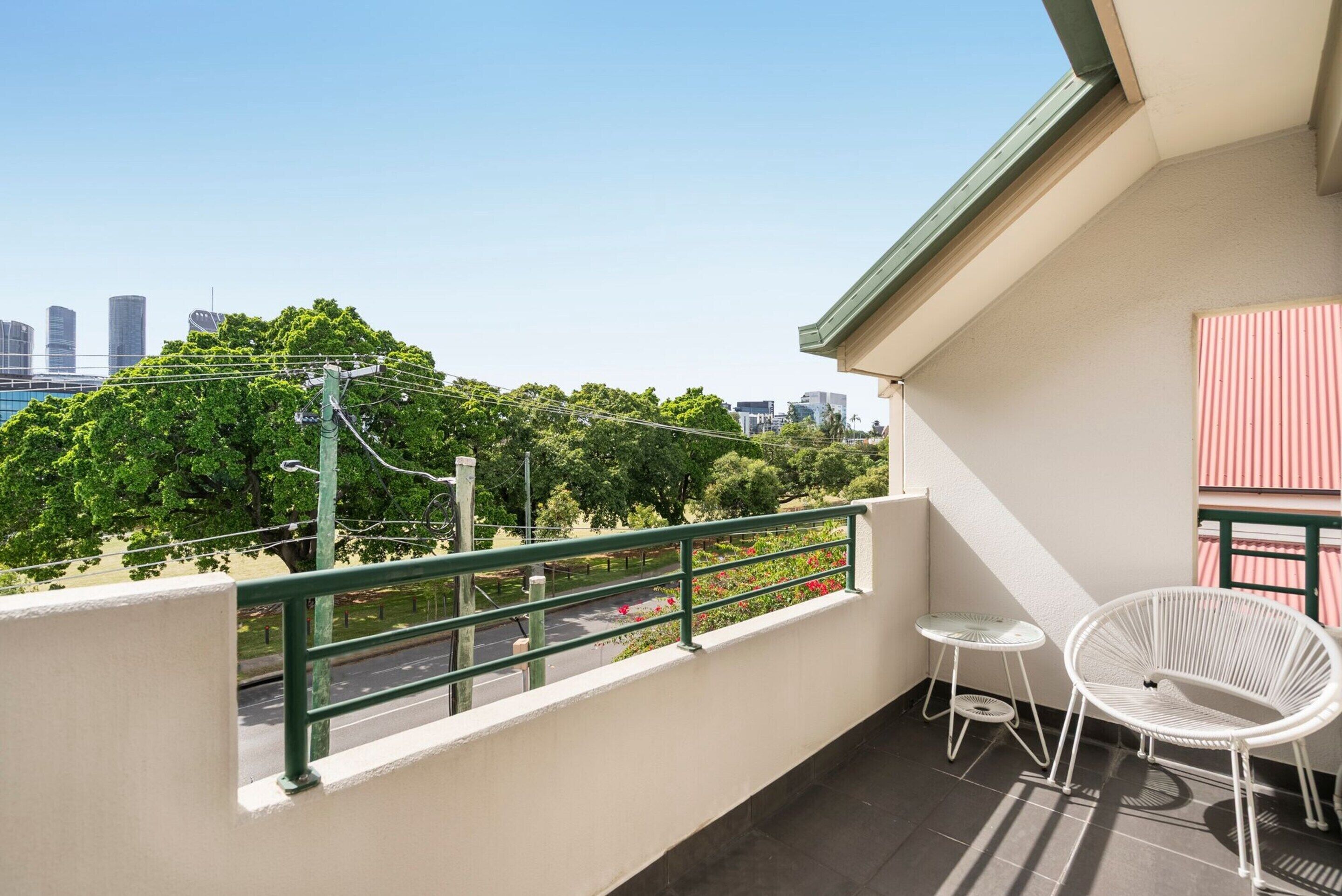 A balcony with a view of a cityscape, a white chair, and a small table.