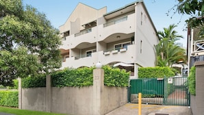 Um edifício residencial com vários andares, varandas, um muro de concreto com um número e um portão verde.