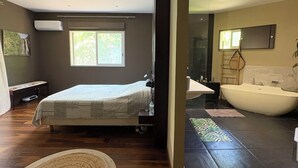 A modern bedroom with a large bed, a window, an air conditioning unit, and a bathroom with a bathtub. - Luxury villa facing the Etang salé les bains beach (L'Étang-Salé)