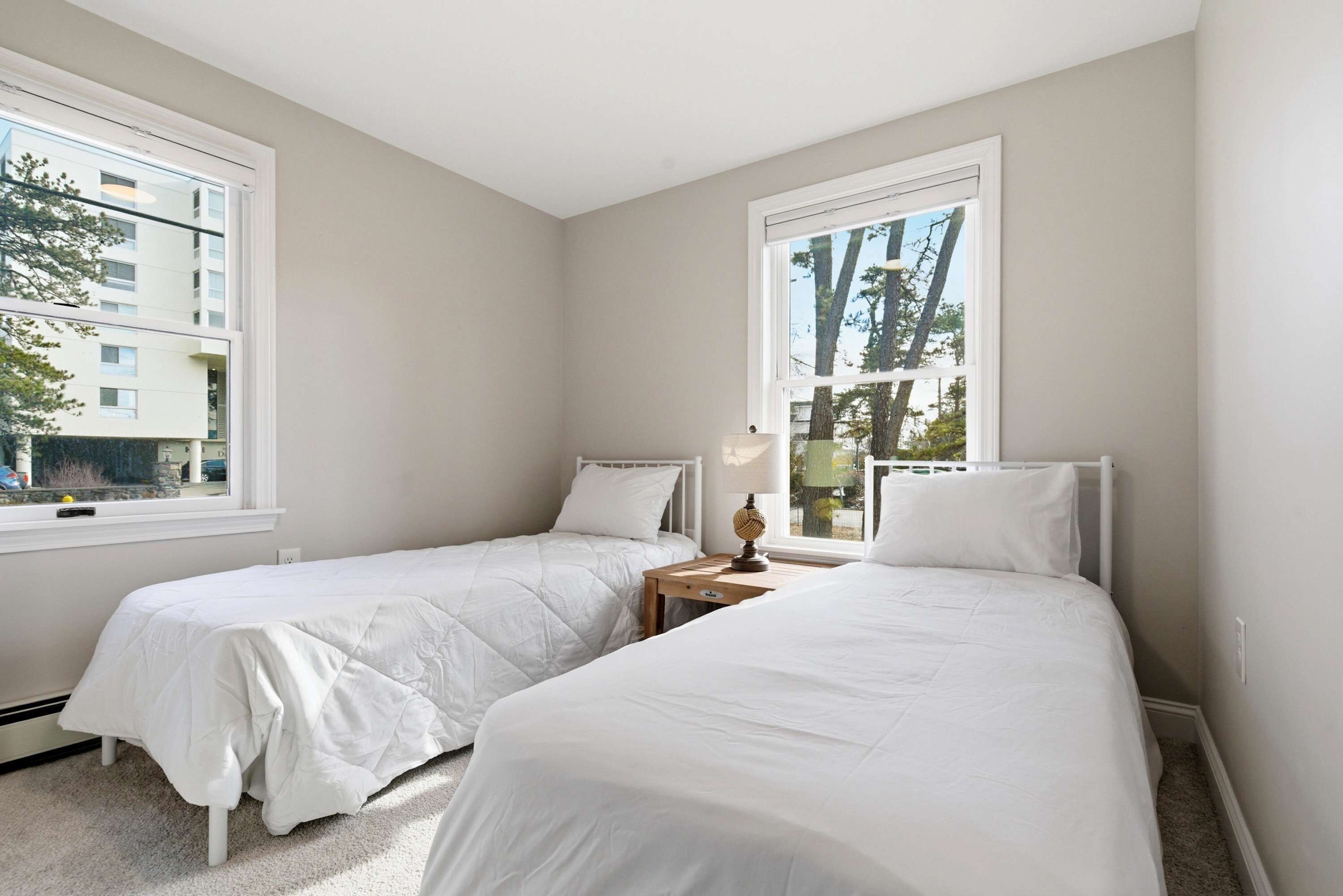 A bedroom with two beds, a window, and a nightstand with a lamp.