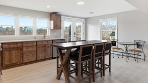A modern kitchen with wooden cabinets, a dining table, and chairs. - Drift Cottage Steps to Beach (Old Orchard Beach)
