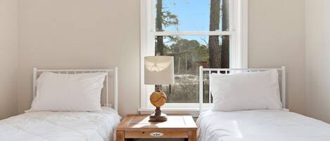 A bedroom with two beds, a nightstand with a lamp, and a window with a view of trees.