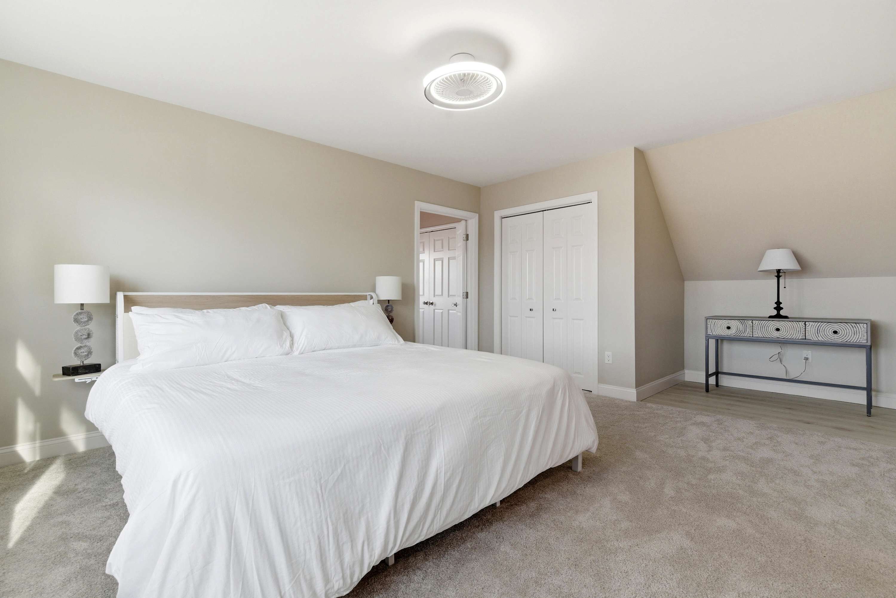 A bedroom with a bed, bedside tables, a desk, and a door.