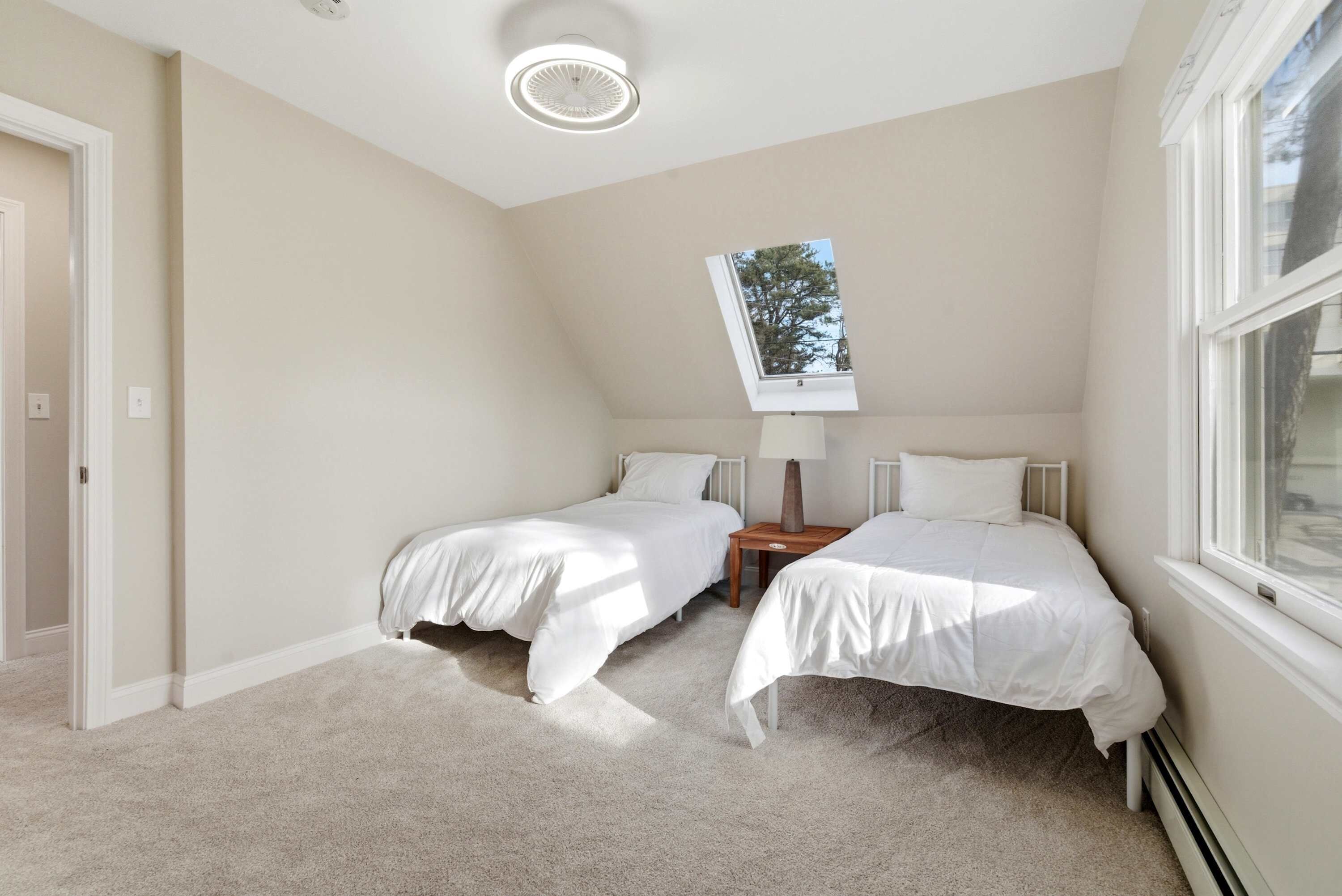 Une chambre avec deux lits simples, un puits de lumière, un luminaire au plafond et une fenêtre.