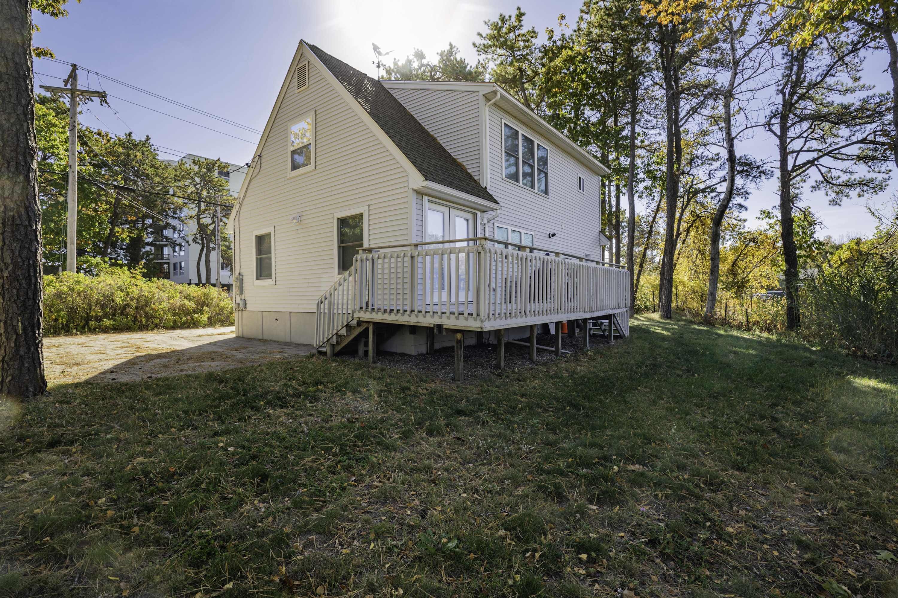 Une maison de plain-pied avec un porche à l’avant et une petite terrasse, entourée d’arbres et d’une pelouse.