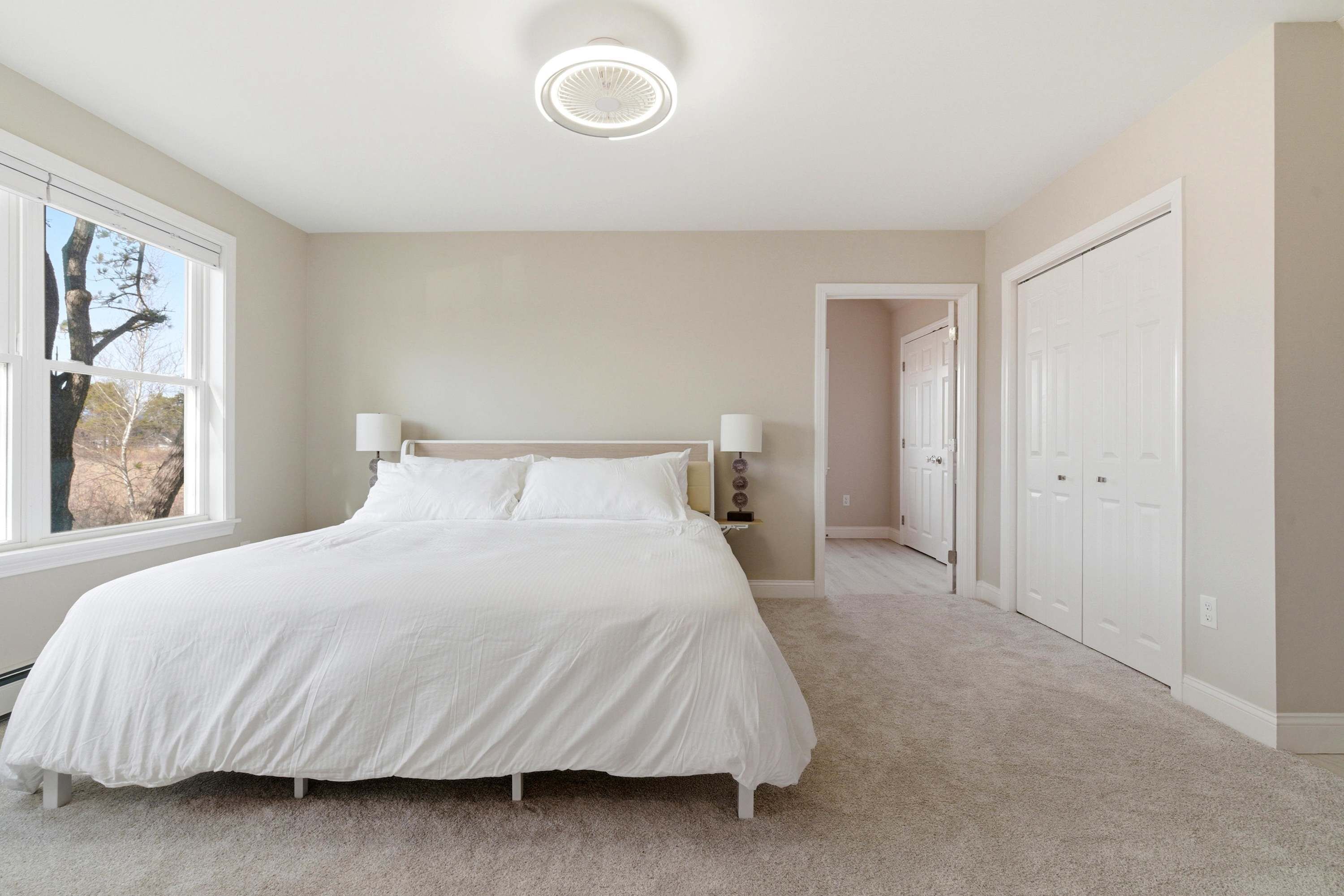 A bedroom with a large bed, a ceiling light, a window, and a door leading to another room.