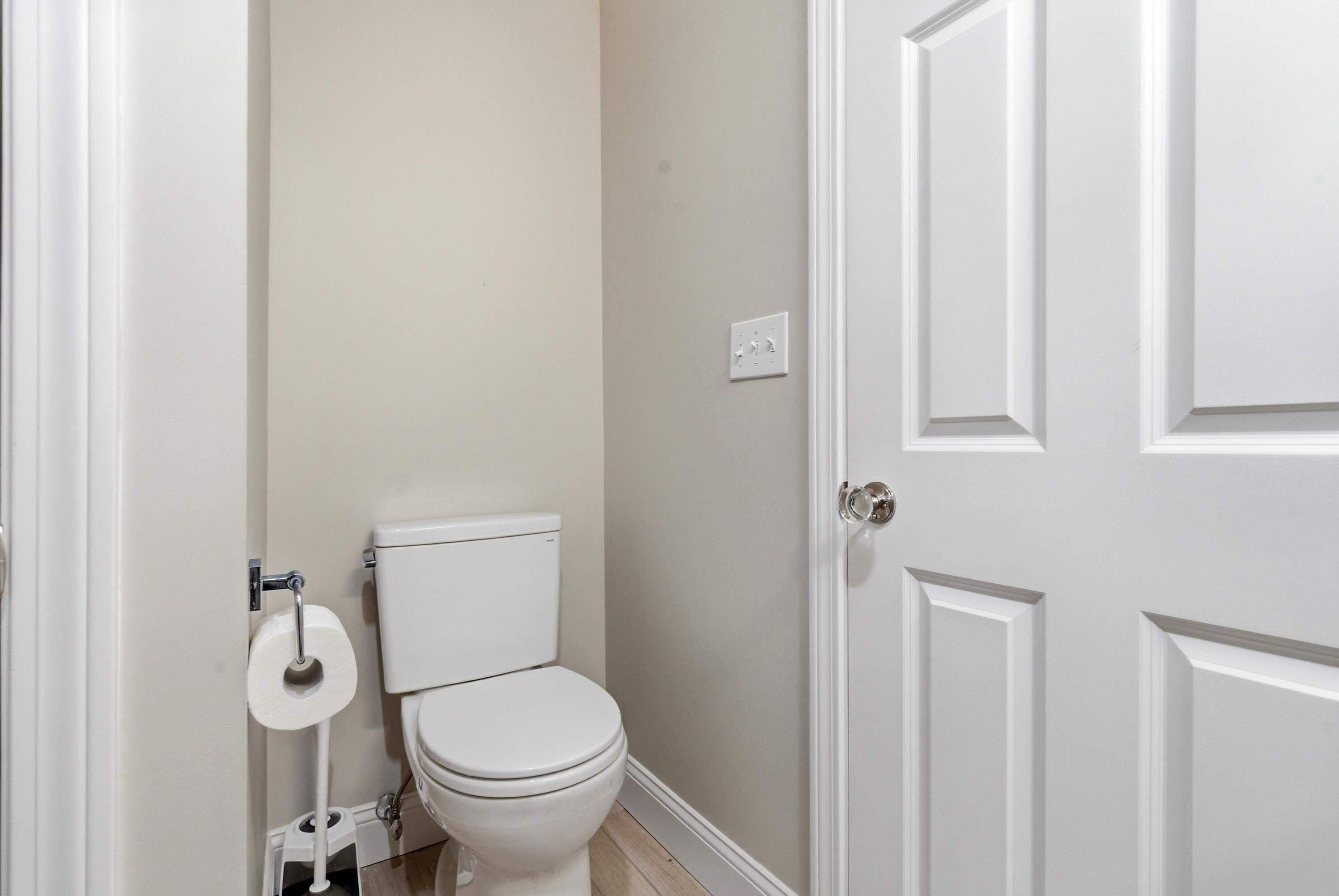 A bathroom with a toilet, a roll of toilet paper, and a door.