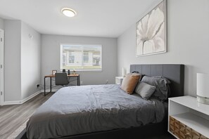 Ein Schlafzimmer mit Bett, Nachttisch, Lampe und Schreibtisch mit Stuhl.