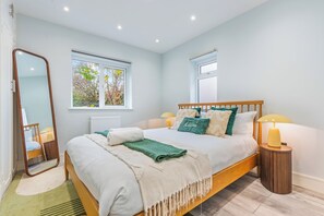 A bedroom with a bed, bedside lamps, a mirror, and windows. - Elephant & Castle Home 3BR/1.5BA with Garden & Pool Table – Central London (London)