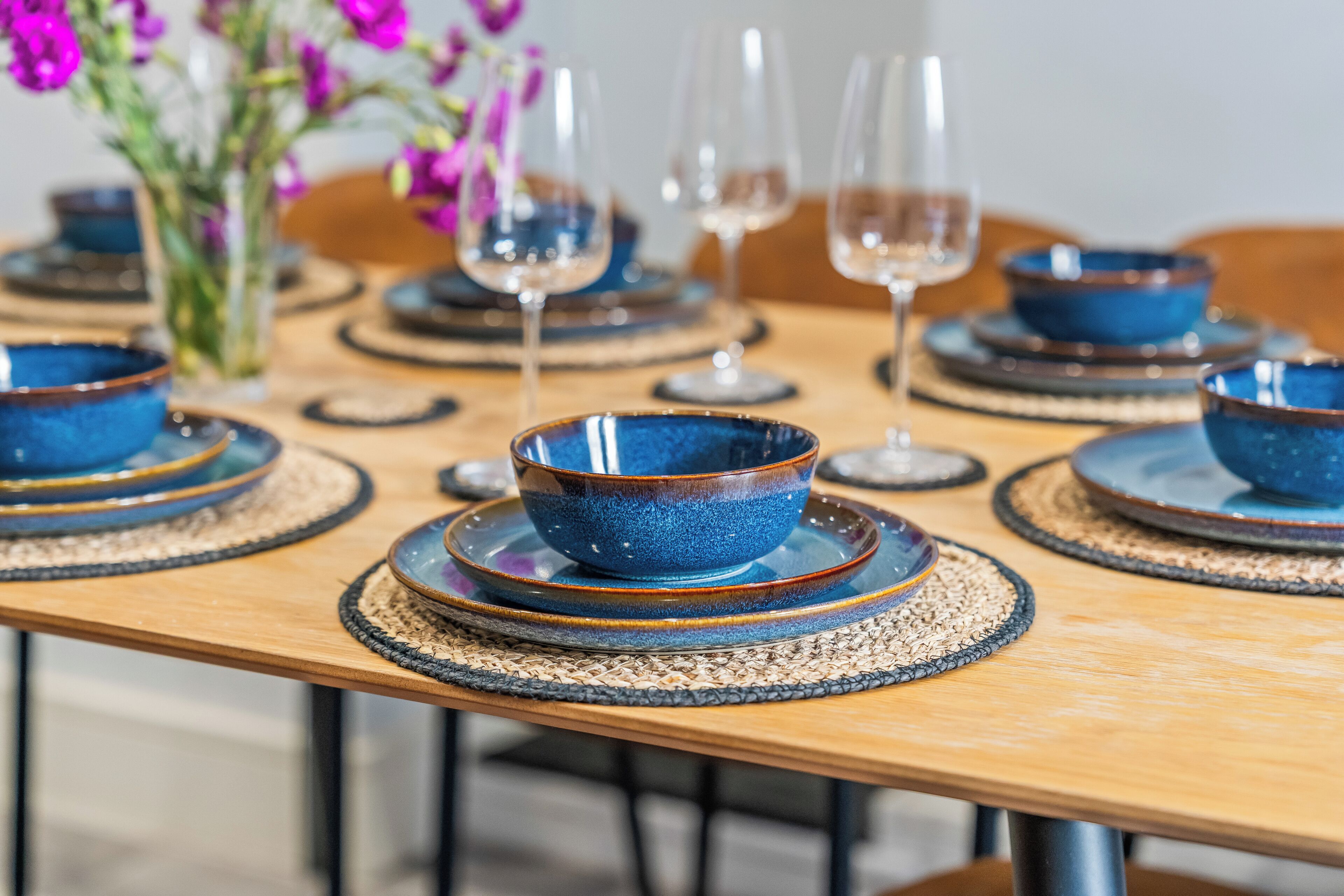 A dining table with blue bowls and wine glasses set for a meal.