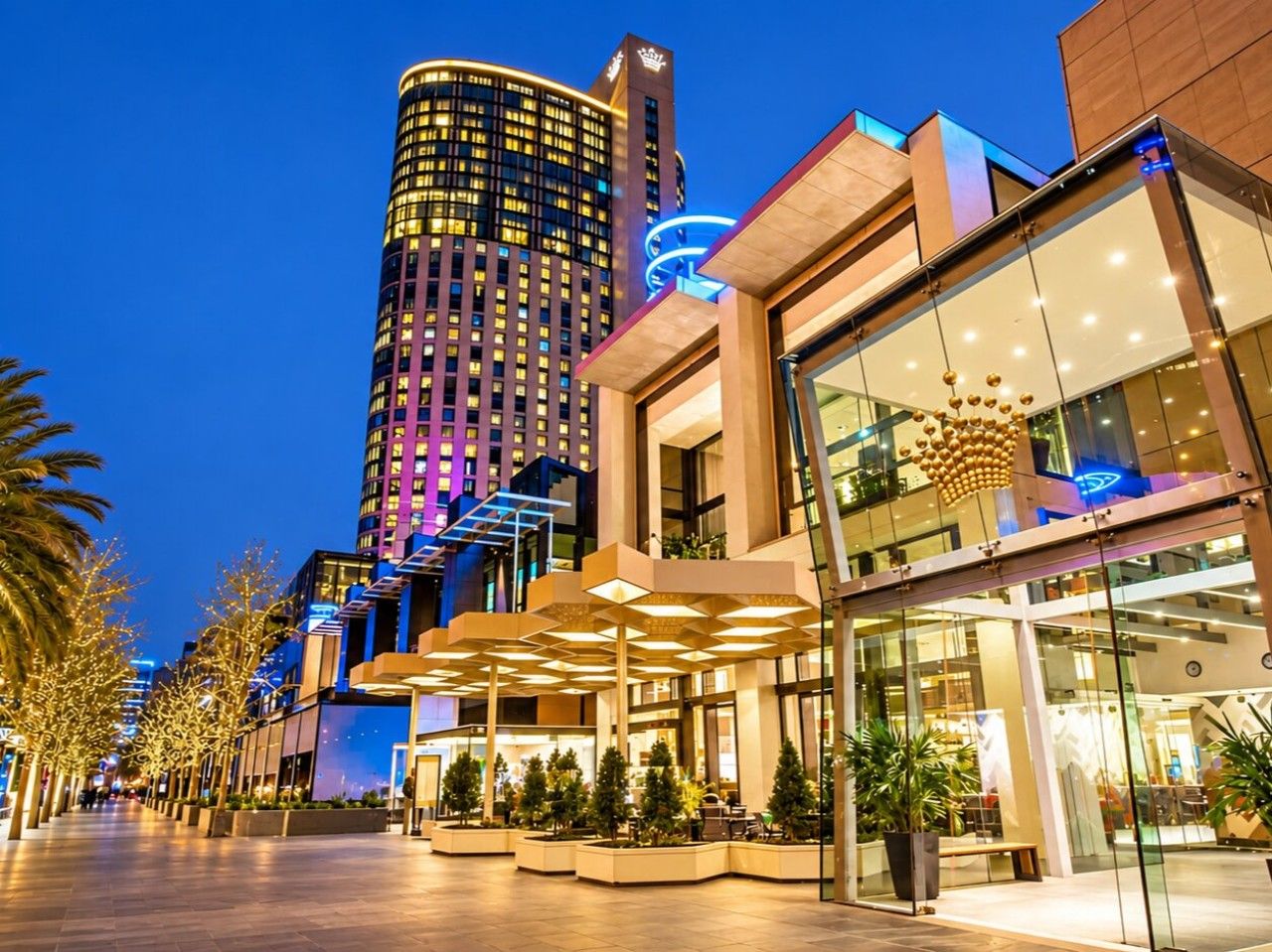 Ein modernes Hotel mit Glasfassade, Außenbereich zum Sitzen und einem Hochhaus im Hintergrund.