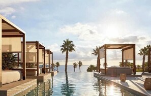 A poolside area with lounge chairs and umbrellas, palm trees, and a clear sky. - MarLau Macenas (Mojacar)