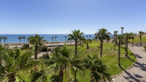 Vista costera con palmeras, cielo despejado y un camino que lleva a la playa.