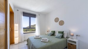Un dormitorio con cama, mesitas de noche, ventana con cortinas y vistas al exterior.
