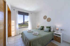 Ein Schlafzimmer mit einem Bett, Nachttischen, einem Fenster mit Vorhängen und Blick ins Freie.