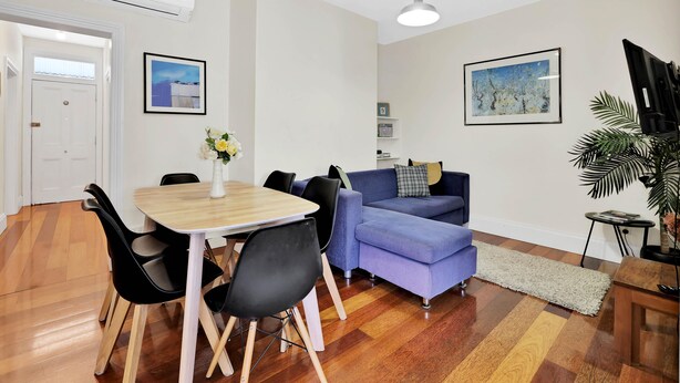 A living room with a dining table, chairs, a sofa, a TV, and a plant.