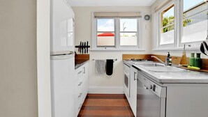 A compact kitchen with white cabinets, a stove, a sink, and a window with a view of the outside.