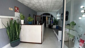 Un espace d’accueil comprenant un comptoir, des plantes en pot, un distributeur automatique et une porte vitrée donnant sur une autre pièce.