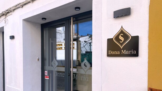 Une devanture de magasin avec une porte vitrée, une enseigne indiquant « Dona Maria » et un logo en forme de losange.