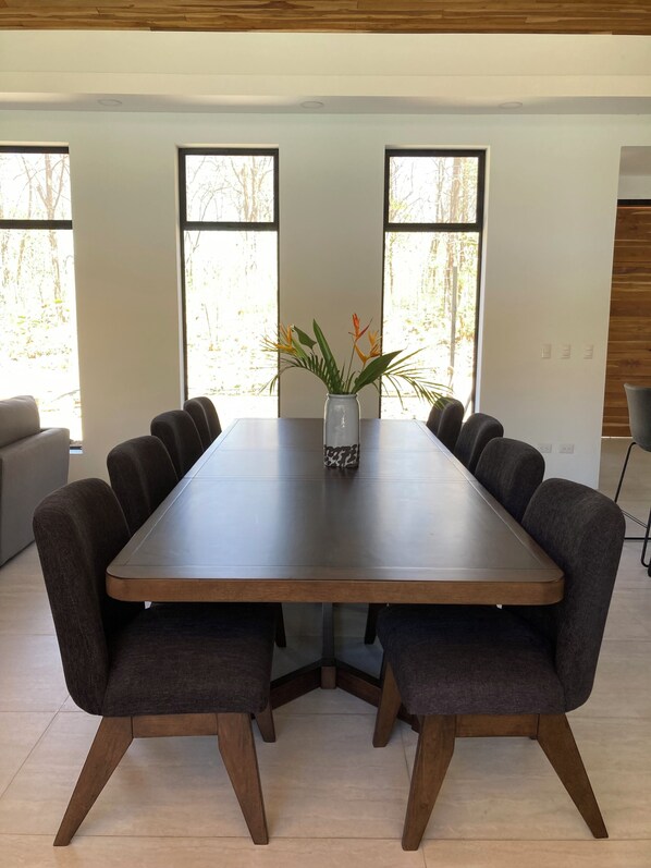 A modern dining area with a rectangular table, dark upholstered chairs, and a vase with plants. - A Private Sanctuary in Playa Avellanas (Guanacaste Province)